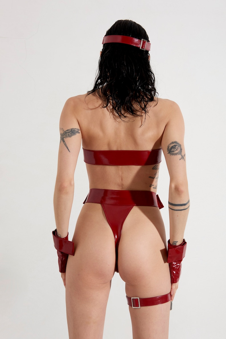 Puede incluir: Un body rojo de charol con pierna alta y cintur&oacute;n ancho. El body tiene un top sin tirantes y pu&ntilde;os y correa de muslo a juego.