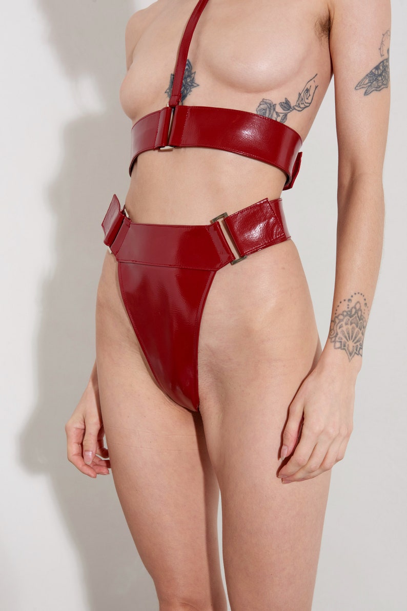 Puede incluir: Ropa interior de talle alto de cuero rojo patentado con una hebilla dorada y una pierna de corte alto.