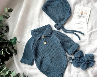 May include: A blue knitted baby outfit set including a hat, bodysuit, and booties. The set is made of soft, comfortable material and features a classic design.