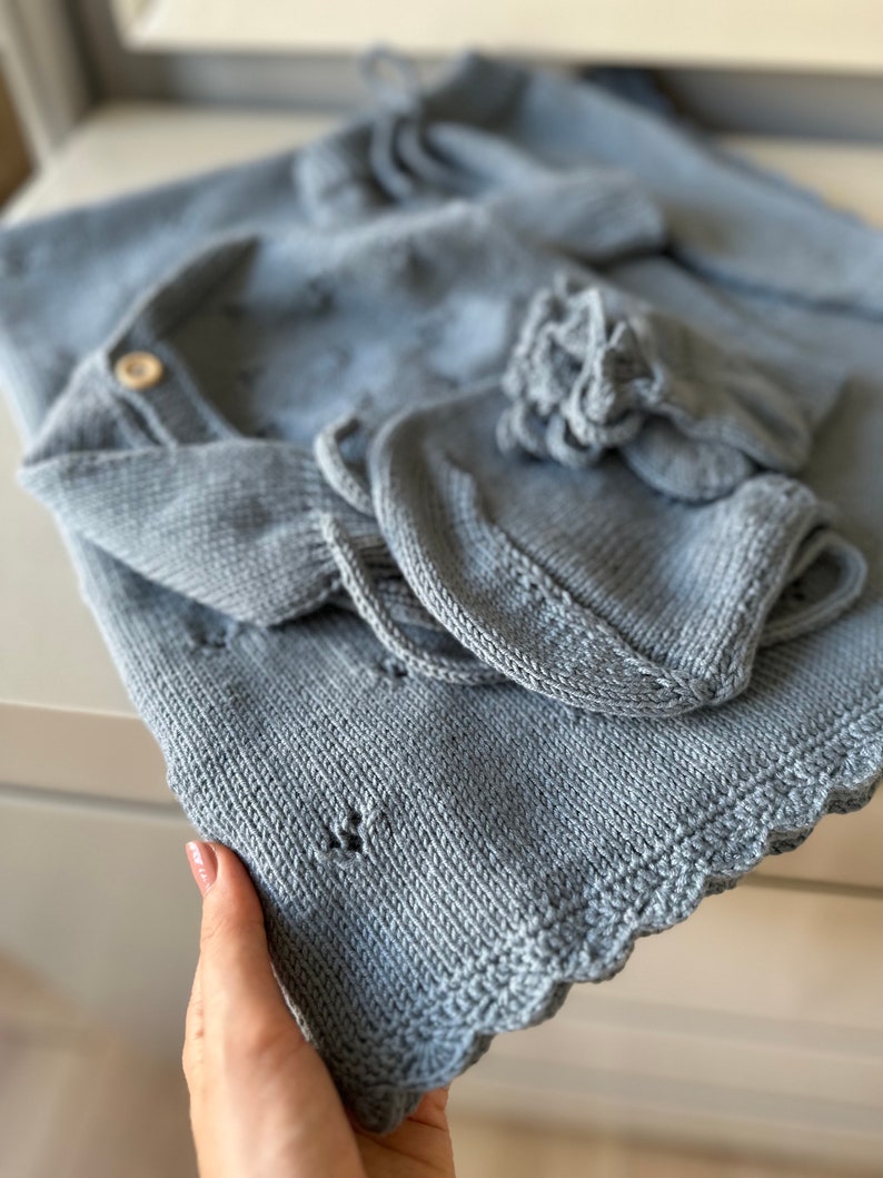 K&ouml;nnte beinhalten: Ein hellblaues gestricktes Baby-Outfit mit einem gewellten Rand. Das Outfit beinhaltet eine M&uuml;tze, einen Pullover und eine Hose.