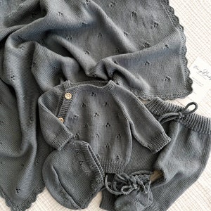 K&ouml;nnte beinhalten: Ein graues gestricktes Baby-Outfit-Set bestehend aus einem Pullover, einer Hose, einer M&uuml;tze und Stiefeln. Das Set ist aus weichem, atmungsaktivem Material gefertigt und hat ein zartes Blumenmuster.