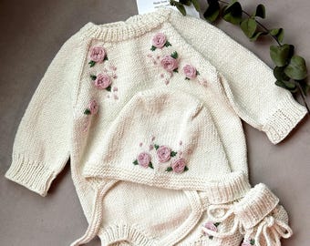 Può includere: Un set di abbigliamento per neonati in maglia color crema con ricamo floreale rosa. Il set comprende un body a maniche lunghe, un cappello e scarpine.