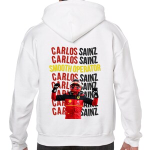 May include: White hooded sweatshirt with a red, black, and yellow graphic print of a race car driver with the text "CARLOS SAINZ" repeated multiple times and "SMOOTH OPERATOR" in between.