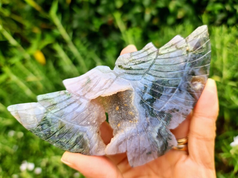 May include: A carved green and purple agate butterfly with a hollow center. The butterfly is carved with intricate details and has a natural crystal formation.
