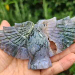 May include: A green and purple agate carving of an eagle with its wings spread. The carving is detailed and intricate, with the agate's natural patterns adding to the beauty of the piece.