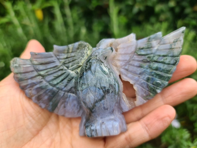 May include: A green and purple agate carving of an eagle with its wings spread. The carving is detailed and intricate, with the agate's natural patterns adding to the beauty of the piece.