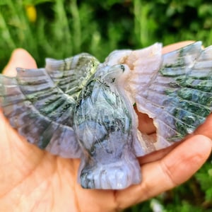 May include: A green and purple agate carving of a bird with its wings spread. The carving is detailed and intricate, with a natural, polished finish.