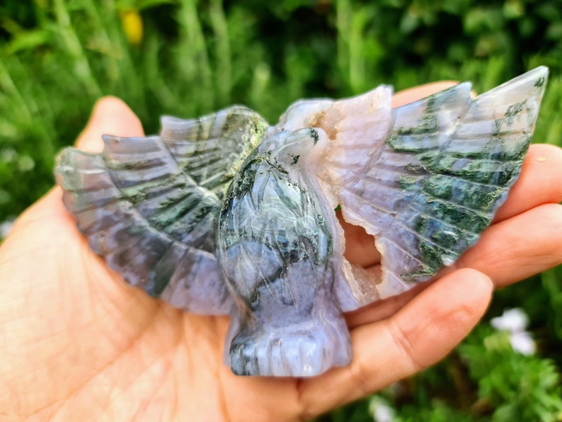 May include: A green and purple agate carving of a bird with its wings spread. The carving is detailed and intricate, with a natural, polished finish.