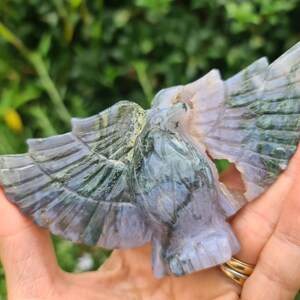 May include: A green and purple agate carving of a bird with its wings spread. The carving is detailed and intricate, with a natural, polished finish.