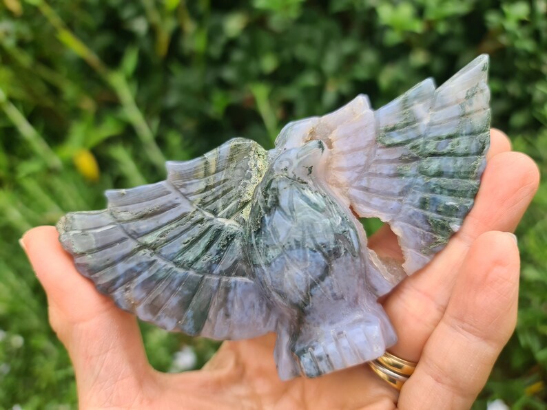May include: A green and purple agate carving of a bird with its wings spread. The carving is detailed and intricate, with a natural, polished finish.