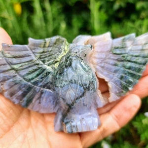 May include: A carved green and purple agate eagle figurine. The eagle has its wings spread out and is detailed with intricate carvings.