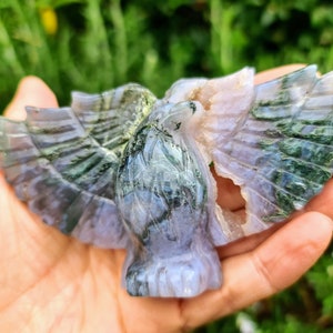 May include: A green and purple agate carving of a bird with its wings spread. The carving is detailed and intricate, with a natural, polished finish.