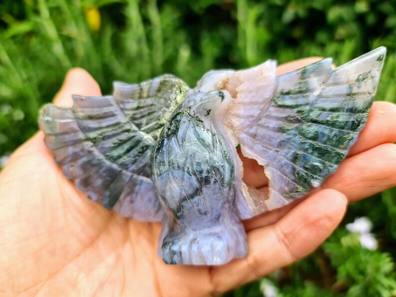 May include: A green and purple agate carving of a bird with its wings spread. The carving is detailed and intricate, with a natural, polished finish.
