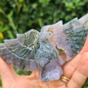 May include: A carved green and purple agate eagle figurine with wings outstretched. The eagle is detailed with intricate patterns and textures.