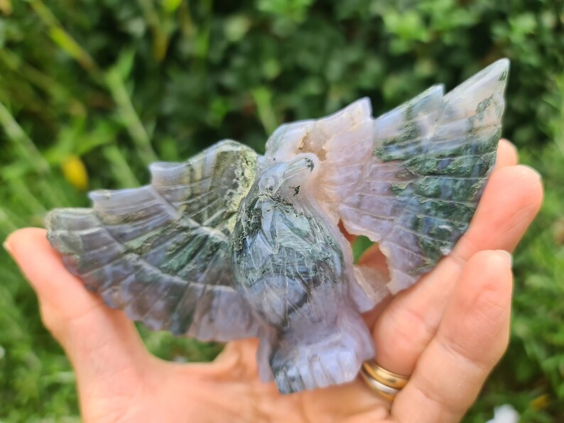 May include: A carved green and purple agate eagle figurine with wings outstretched. The eagle is detailed with intricate patterns and textures.