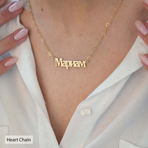 May include: A gold necklace with a heart chain and a nameplate pendant that reads "Mariam".