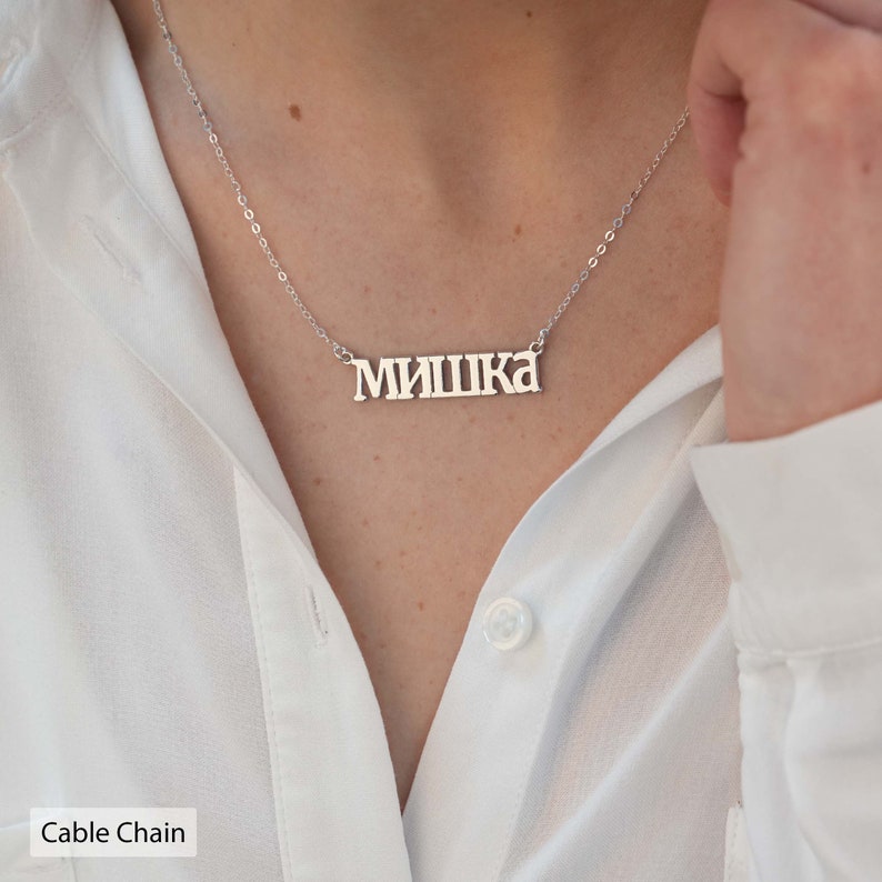 May include: A silver necklace with a nameplate pendant that reads "МИШКА" in Cyrillic script. The necklace is on a cable chain.