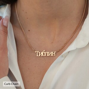 May include: A gold curb chain necklace with a personalized nameplate that reads "Тиблин".