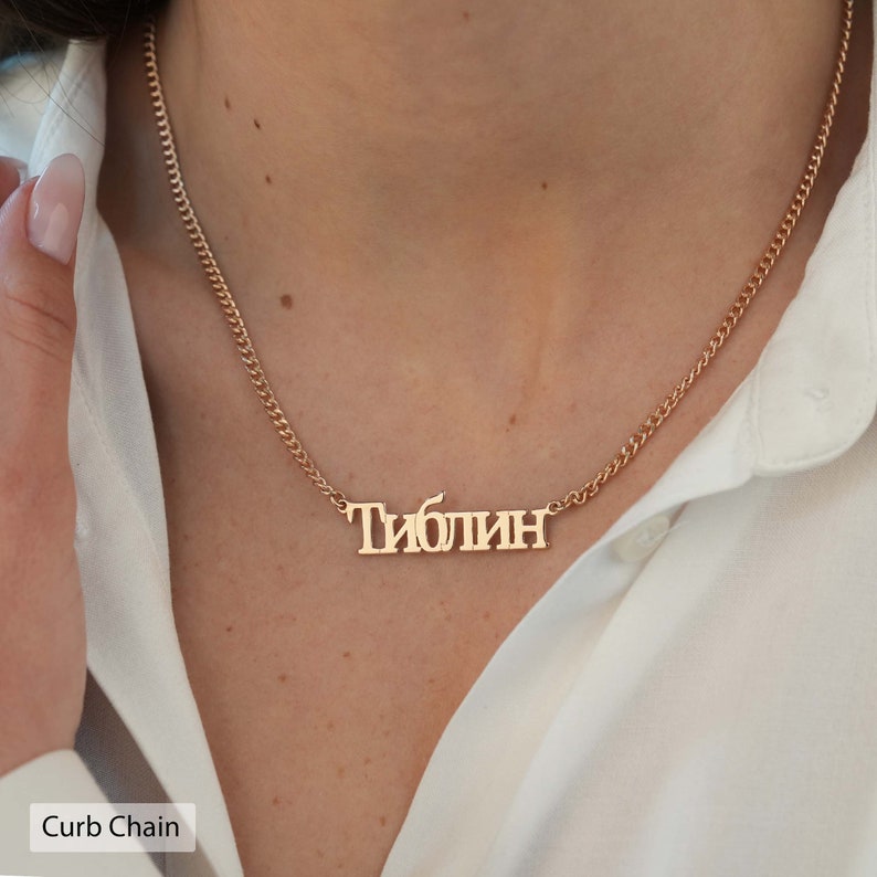 May include: A gold curb chain necklace with a personalized nameplate that reads "Тиблин".