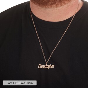 Puede incluir: Un collar dorado con un colgante de placa con el nombre "Christopher" escrito en cursiva. El collar tiene un estilo de cadena rolo.