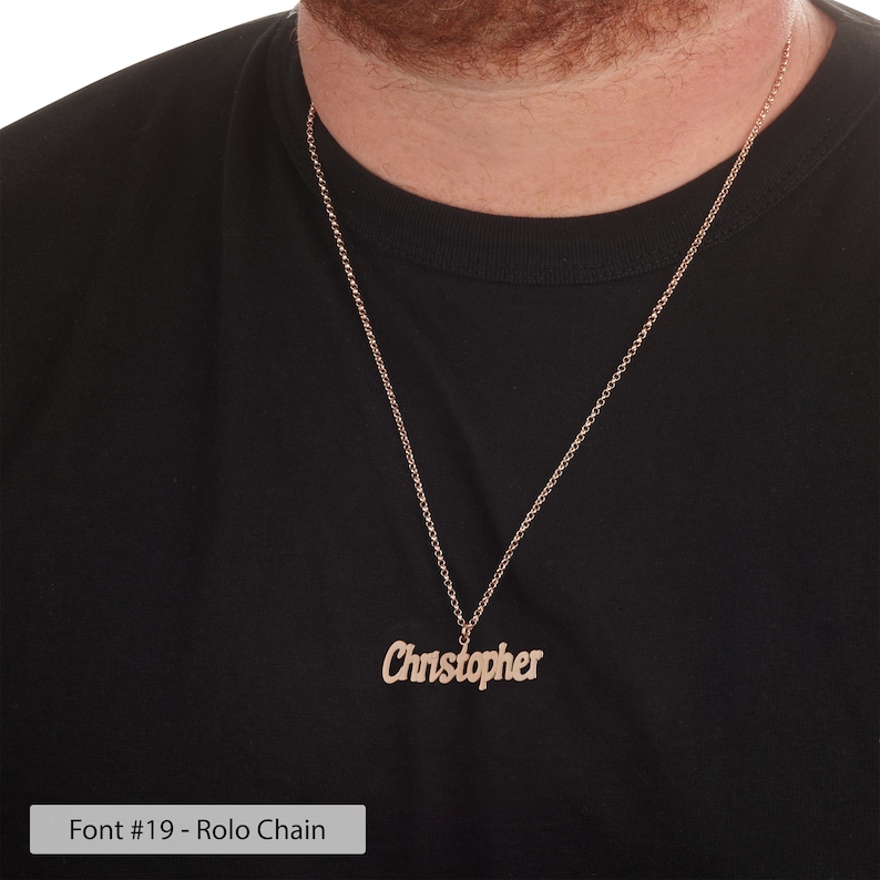 Puede incluir: Un collar dorado con un colgante de placa con el nombre "Christopher" escrito en cursiva. El collar tiene un estilo de cadena rolo.