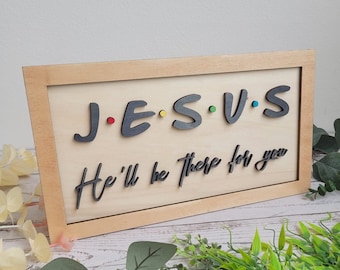 Pode incluir: Uma placa de madeira com uma moldura marrom clara e um fundo de madeira claro. A placa diz "J.E.S.U.S. He'll be there for you" em letras pretas com pontos coloridos entre as letras.