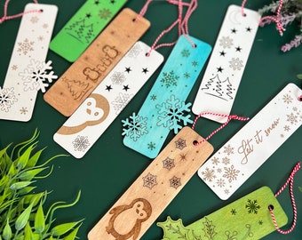 May include: A collection of wooden bookmarks with various winter-themed designs. The bookmarks feature snowflakes, penguins, Christmas trees, and holly. Each bookmark has a red and white string for easy use. The color palette includes natural wood, white, green, and blue.