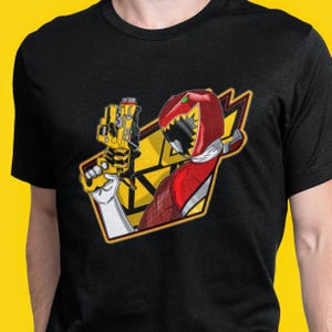 Puede incluir: Camiseta negra con un gráfico rojo y amarillo de un Power Ranger sosteniendo un arma. El gráfico presenta un Power Ranger rojo con un casco de dinosaurio y un arma amarilla.