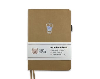 May include: A brown dotted notebook with a cute illustration of a boba tea on the front cover. The notebook is made of soft vegan leather and has 160 pages of bright white paper. It is a washi wombat product.