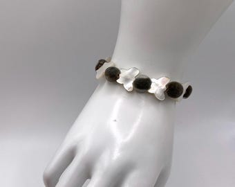 May include: A bracelet featuring alternating white mother-of-pearl butterfly-shaped beads and dark brown, rounded, textured stone beads. The beads are strung together in a repeating pattern to form a circular band that encircles the wrist area.