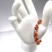 A copper-colored bracelet made of interwoven wire, creating a chain-like design. The bracelet is displayed on a white mannequin hand.
