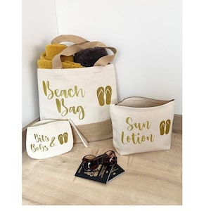 May include: Three canvas bags with gold lettering and flip-flop icons. The largest bag says "Beach Bag", the medium bag says "Bits & Bobs", and the smallest bag says "Sun Lotion".