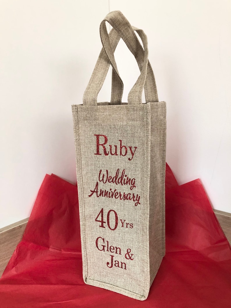 May include: A beige linen wine bottle gift bag with red embroidered text that reads "Ruby Wedding Anniversary 40 Yrs Glen & Jan".