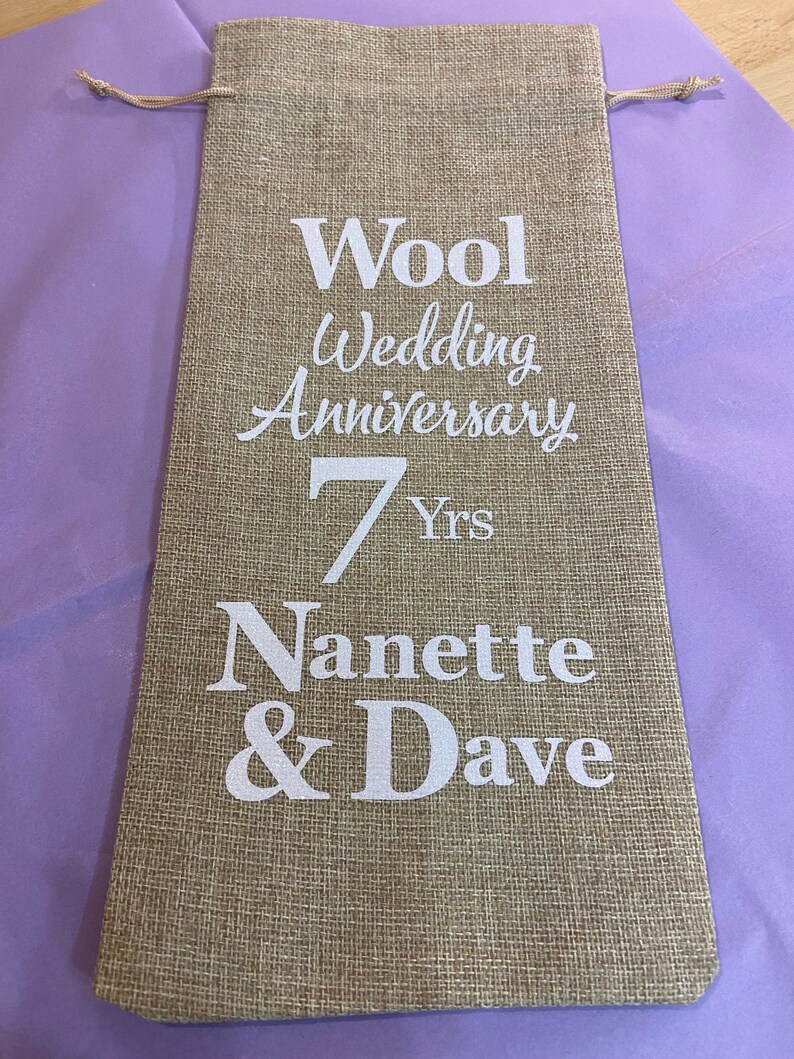 May include: A brown burlap bag with a white drawstring. The bag has white text that reads "Wool Wedding Anniversary 7 Yrs Nanette & Dave".