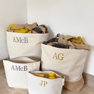 K&ouml;nnte beinhalten: Vier Canvas-Taschen mit personalisierten Initialen. Zwei gro&szlig;e Tragetaschen mit braunen Griffen, eine mit den Initialen "AG" und die andere mit "AMcB". Zwei kleinere Rei&szlig;verschlusstaschen, eine mit "AMcB" und die andere mit "JP".