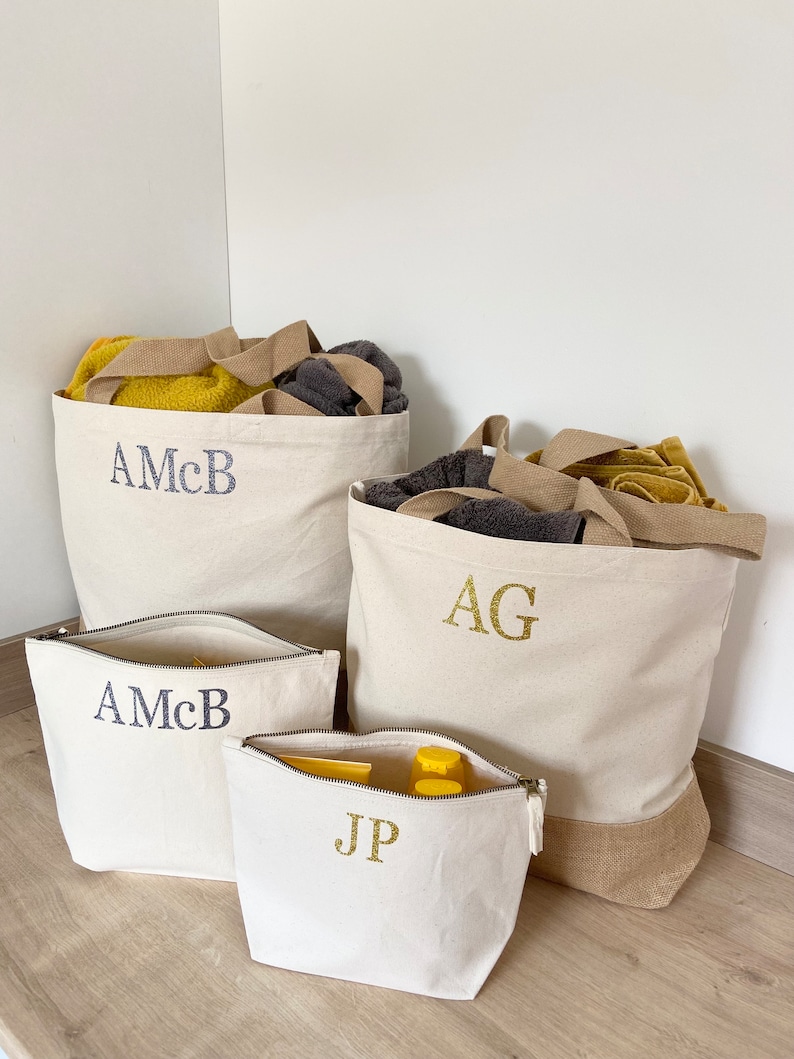 K&ouml;nnte beinhalten: Vier Canvas-Taschen mit personalisierten Initialen. Zwei gro&szlig;e Tragetaschen mit braunen Griffen, eine mit den Initialen "AG" und die andere mit "AMcB". Zwei kleinere Rei&szlig;verschlusstaschen, eine mit "AMcB" und die andere mit "JP".
