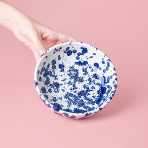 May include: A white ceramic bowl with a blue and white splatter pattern. The bowl has a textured surface and is perfect for serving.