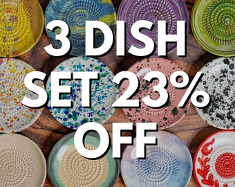 Pode incluir: Uma coleção de onze pratos raladores de cerâmica circulares com vários padrões e cores, incluindo pintura salpicada, motivos florais e centros texturizados. O texto 3 DISH SET 23% OFF está sobreposto em letras brancas no centro da imagem.
