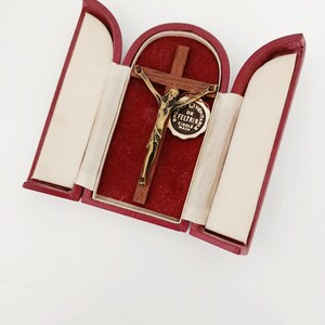 Peut inclure: Un crucifix vintage dans un étui rouge. Le crucifix présente une figure de Jésus dorée sur une croix en bois. L'étui est ouvert, révélant un intérieur en velours rouge et une doublure crème. Le texte "DE FELTRIN" est visible.