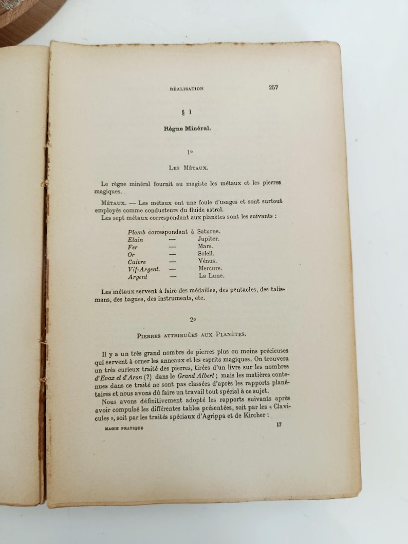May include: Open book with aged, yellowed pages. Text in French includes the title "R&egrave;gne Min&eacute;ral" and lists metals and their planetary correspondences. The page is from a book on magic.