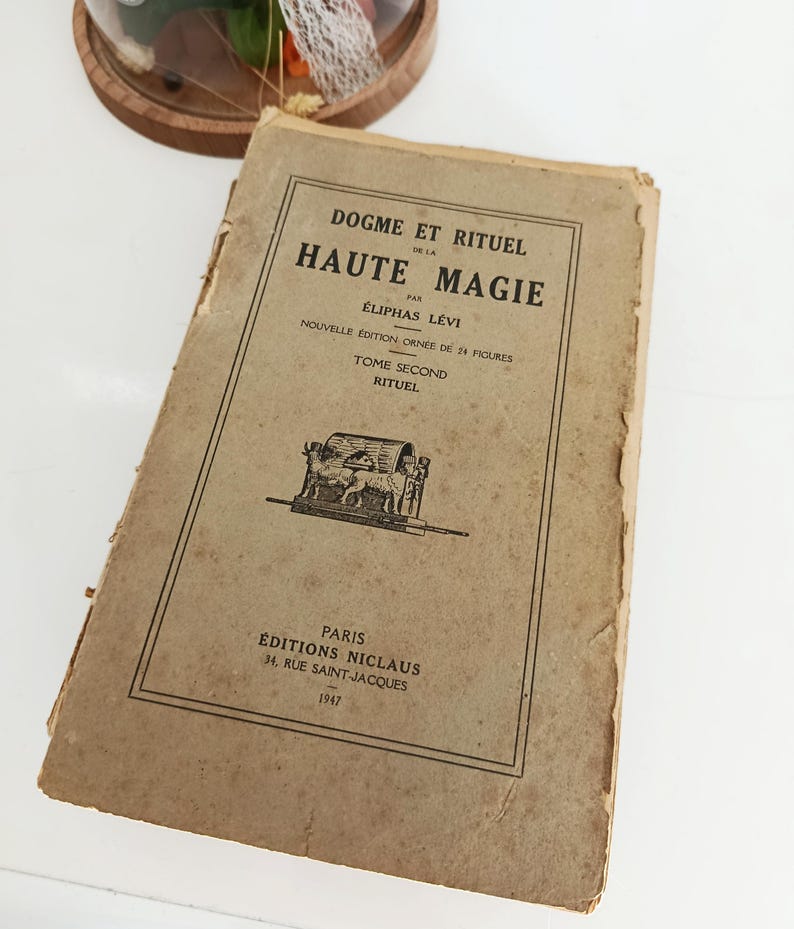 May include: A vintage book titled "DOGME ET RITUEL DE LA HAUTE MAGIE" by &Eacute;liphas L&eacute;vi. The cover is a faded tan color with black text and illustrations. The book is a second edition, published in Paris in 1947.