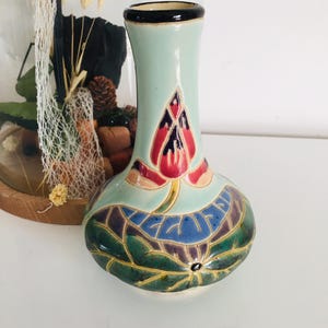 Peut inclure: Un petit vase en céramique bleu et vert avec un motif floral. Le vase a une base large et un col étroit. Le motif floral présente une fleur de lotus rouge avec des feuilles vertes.