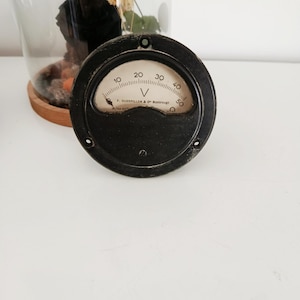 Puede incluir: Un voltímetro negro vintage con una esfera blanca y una aguja que indica una lectura. La esfera muestra números del 10 al 50, con la letra "V" en el centro. El texto "F. GUERPILLON & C° Montrouge" está impreso debajo.