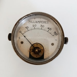 Può includere: Un milliamperometro rotondo vintage con quadrante bianco e lancetta nera. Il quadrante mostra la parola "MILLIAMPERES" e numeri da 10 a 50. Il misuratore ha un involucro in metallo e due manopole di regolazione. L'ago punta a circa 10.