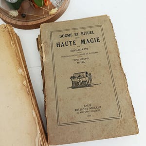 May include: Vintage book titled "Dogme et Rituel de la Haute Magie" by &Eacute;liphas L&eacute;vi. The cover is tan with black text and illustrations. The book is from the &Eacute;ditions Niclaus, Paris, 1947. The book is aged with worn edges.