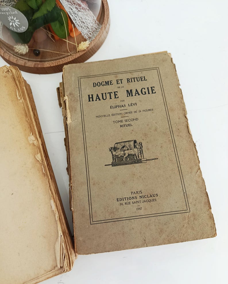 May include: Vintage book titled "Dogme et Rituel de la Haute Magie" by &Eacute;liphas L&eacute;vi. The cover is tan with black text and illustrations. The book is from the &Eacute;ditions Niclaus, Paris, 1947. The book is aged with worn edges.