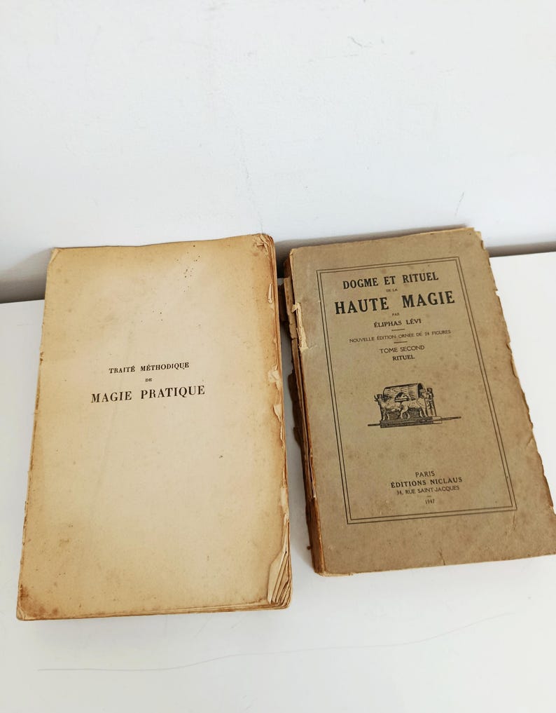 May include: Two antique books with aged, tan covers. The left book reads "TRAIT&Eacute; M&Eacute;THODIQUE DE MAGIE PRATIQUE." The right book is titled "DOGME ET RITUEL DE HAUTE MAGIE" by &Eacute;liphas L&eacute;vi. Both books show signs of wear.