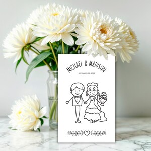 May include: A white wedding invitation card with the names "MICHAEL & MADISON" and the date "SEPTEMBER 26, 2026". The card features a black and white illustration of a bride and groom holding hands, with floral and heart accents.