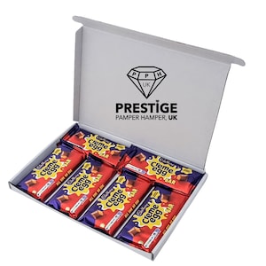 May include: A white box with the text "PRESTIGE PAMPER HAMPER, UK" on the lid. The box is open and contains six Cadbury Creme Egg chocolate bars wrapped in purple foil with a red and yellow design.