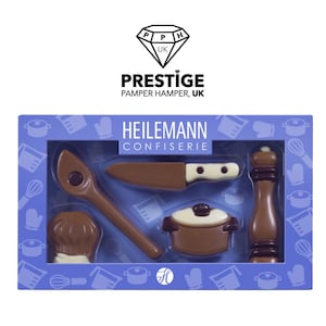 May include: A blue box with a clear window showing a set of chocolate kitchen tools. The tools include a chef's hat, a wooden spoon, a knife, a pot, and a pepper mill. The box has the text "HEILEMANN CONFISERIE" on the top.